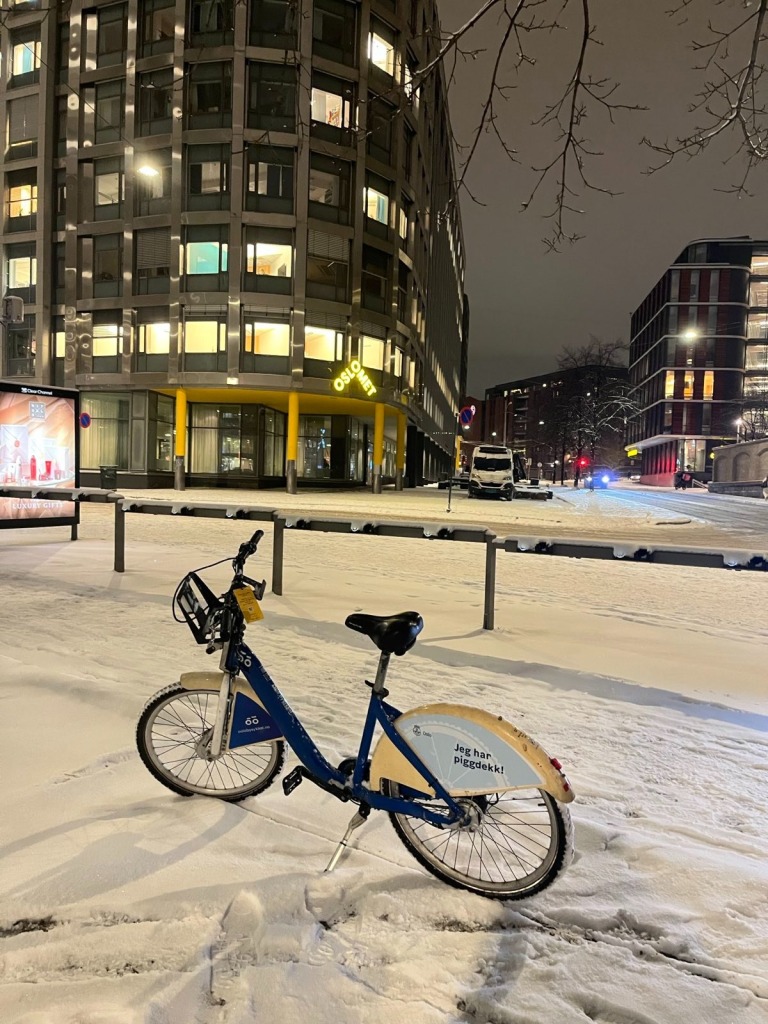 A blue Oslo city bike on a snowy pavement.